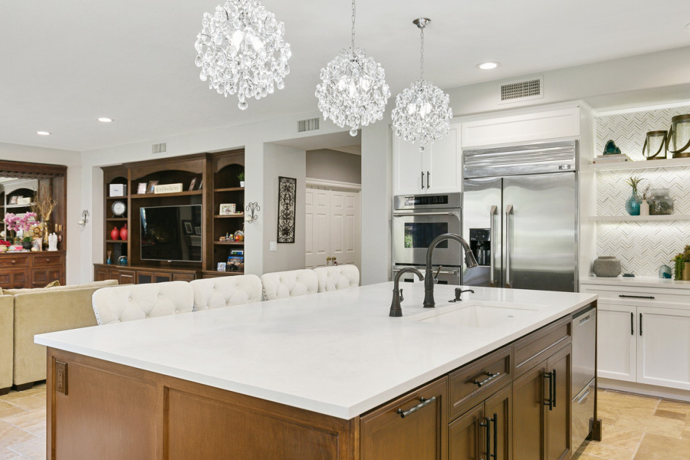 This is an example of a large traditional open plan kitchen in Orange County with a submerged sink, shaker cabinets, white cabinets, engineered stone countertops, beige splashback, glass tiled splashback, stainless steel appliances, travertine flooring, an island, brown floors and white worktops.