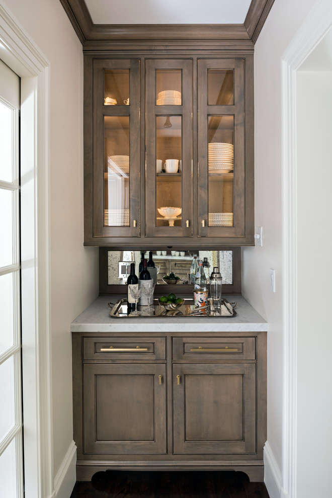 Photo of a small traditional single-wall home bar in Boston with no sink, glass-front cabinets, brown cabinets, mirror splashback and grey benchtop.