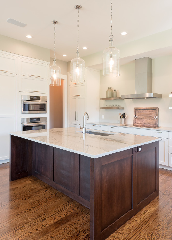 Mid-sized transitional u-shaped open plan kitchen in Other with an undermount sink, shaker cabinets, white cabinets, marble benchtops, stainless steel appliances, dark hardwood floors, with island and brown floor.