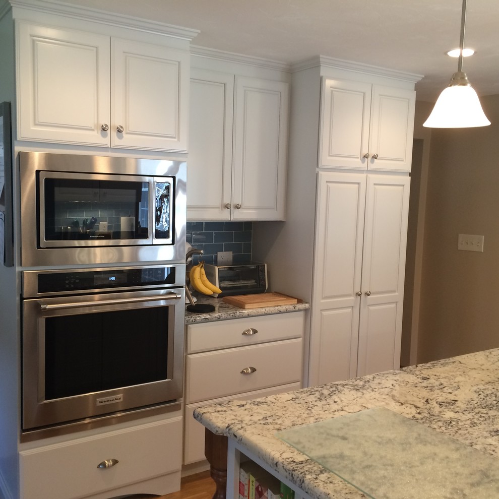 Eat-in kitchen - transitional u-shaped medium tone wood floor eat-in kitchen idea in Boston with an undermount sink, raised-panel cabinets, white cabinets, granite countertops, blue backsplash, glass tile backsplash, stainless steel appliances and an island