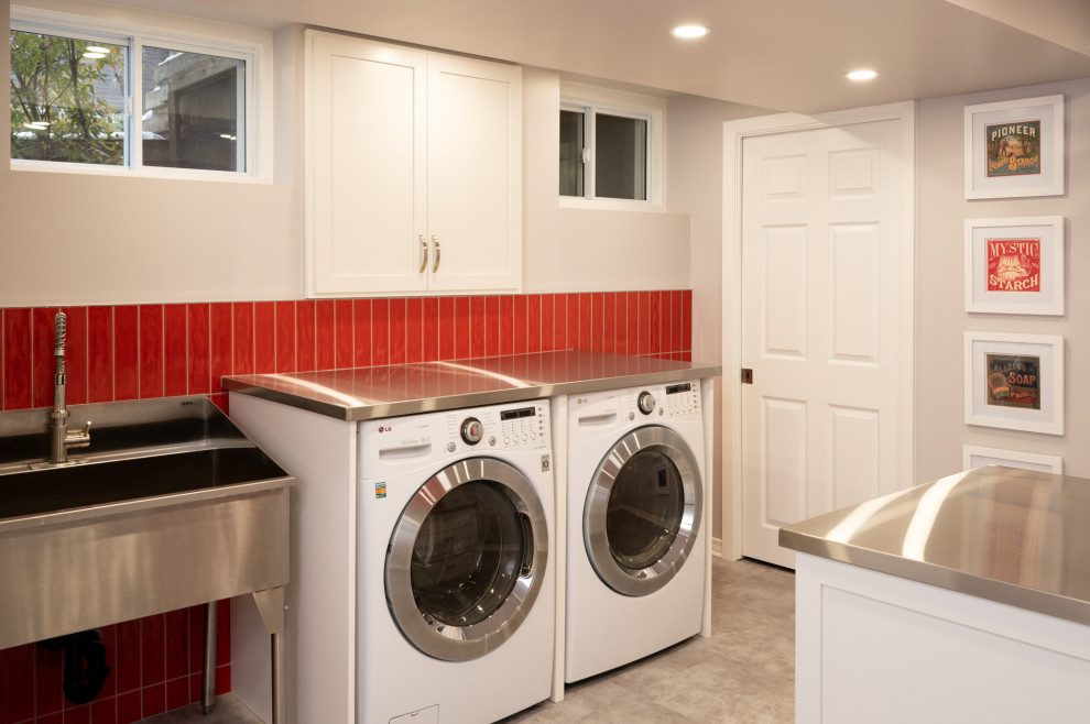 This is an example of a mid-sized contemporary dedicated laundry room in Ottawa with an utility sink, shaker cabinets, white cabinets, stainless steel benchtops, red splashback, subway tile splashback, vinyl floors, a side-by-side washer and dryer, grey floor and white walls.