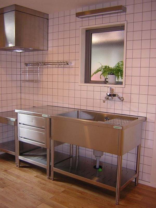 This is an example of a small industrial single-wall separate kitchen in Other with a single-bowl sink, open cabinets, stainless steel cabinets, stainless steel benchtops, metallic splashback, porcelain splashback, white appliances, medium hardwood floors, no island and brown floor.