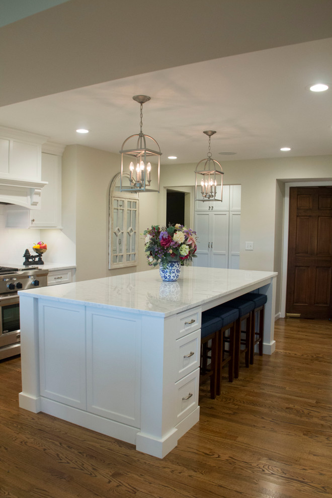 Example of a huge transitional medium tone wood floor open concept kitchen design with an undermount sink, shaker cabinets, white cabinets, marble countertops, white backsplash, ceramic backsplash, stainless steel appliances and two islands