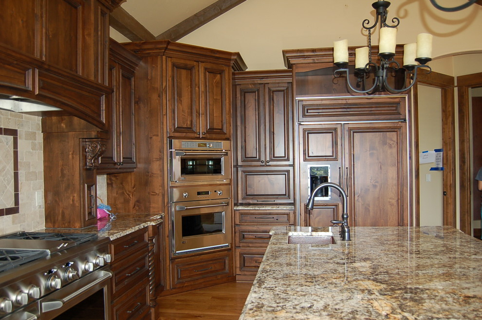 Eat-in kitchen - large rustic u-shaped medium tone wood floor eat-in kitchen idea in Denver with a farmhouse sink, raised-panel cabinets, dark wood cabinets, granite countertops, beige backsplash, ceramic backsplash, stainless steel appliances and an island