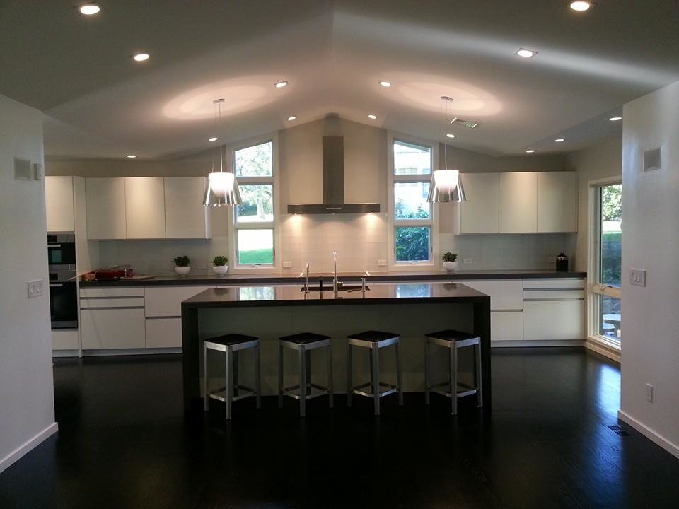 Example of a mid-sized transitional single-wall medium tone wood floor open concept kitchen design in Boston with a drop-in sink, flat-panel cabinets, white cabinets, granite countertops, white backsplash, stone tile backsplash, stainless steel appliances and an island