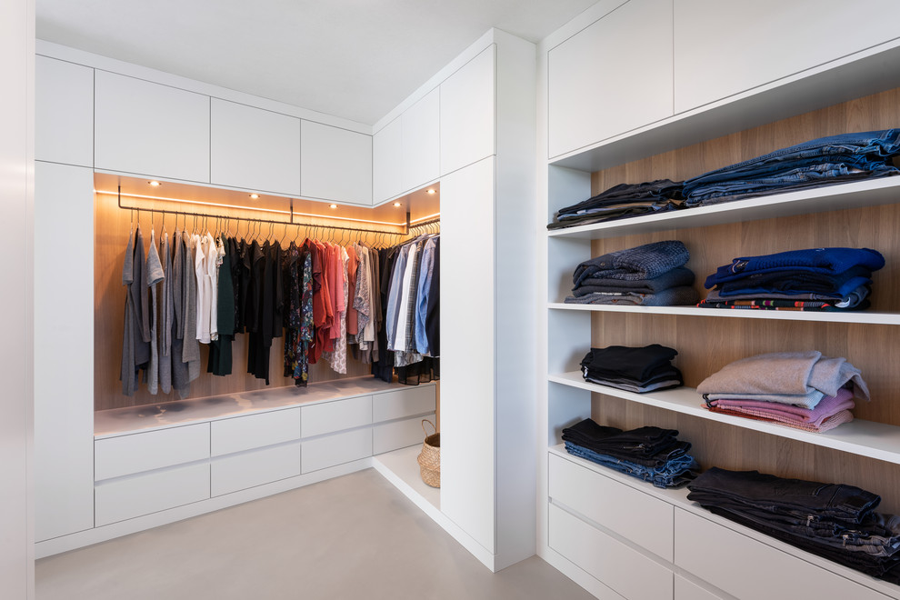 Photo of an expansive scandinavian gender-neutral walk-in wardrobe in Munich with flat-panel cabinets, white cabinets, concrete floors and grey floor.