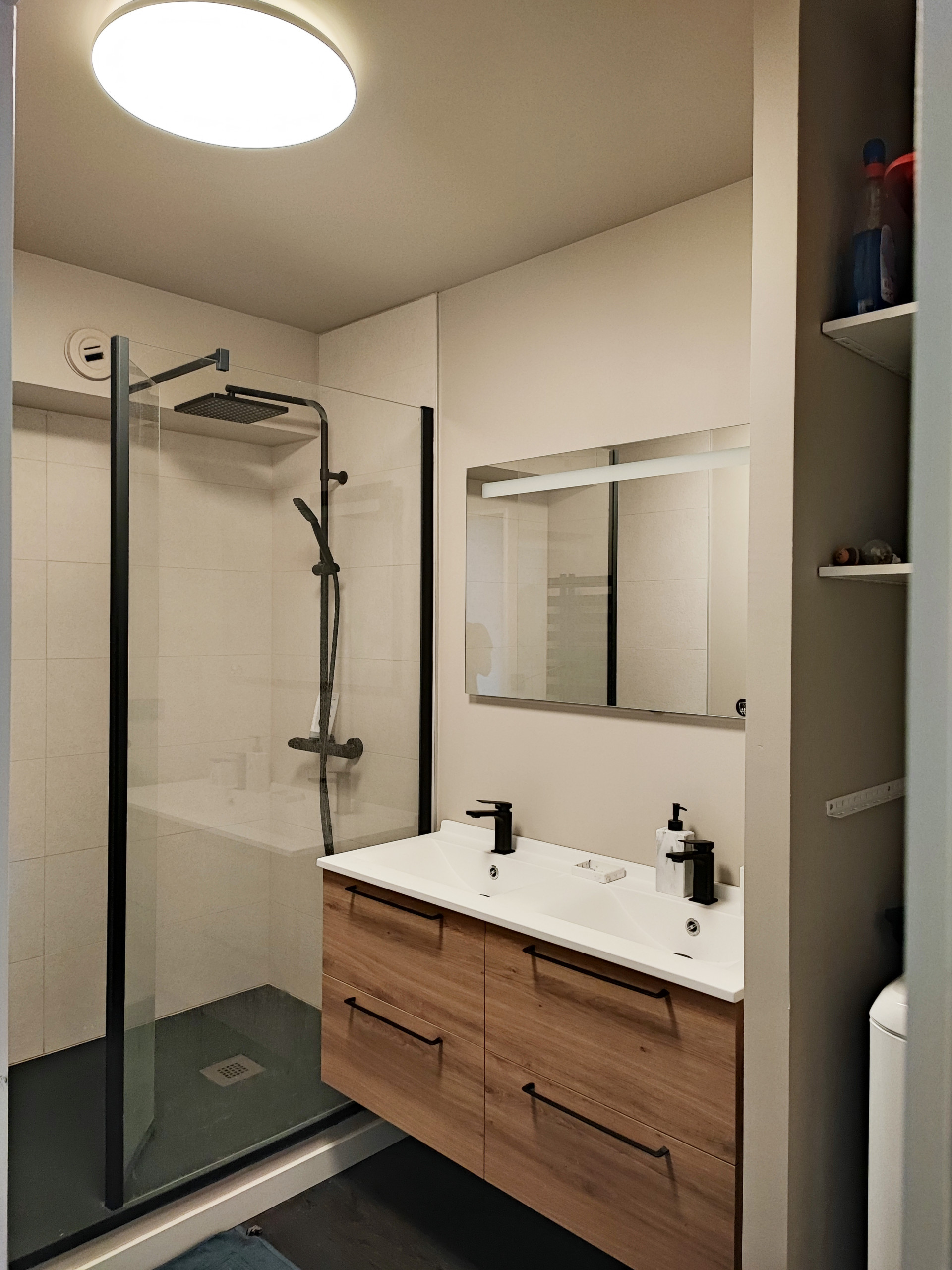 La salle d'eau de l'appartement, servant aussi de buanderie. Un meuble double vasque avec de larges tiroirs permet de maximiser les rangements dans cet espace restreint. La douche est spacieuse. La bu