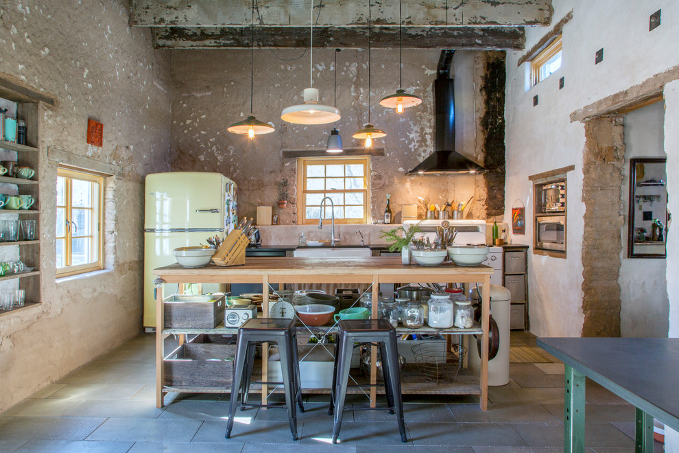 This is an example of an eclectic galley kitchen in Other with a farmhouse sink, coloured appliances, with island and black floor.