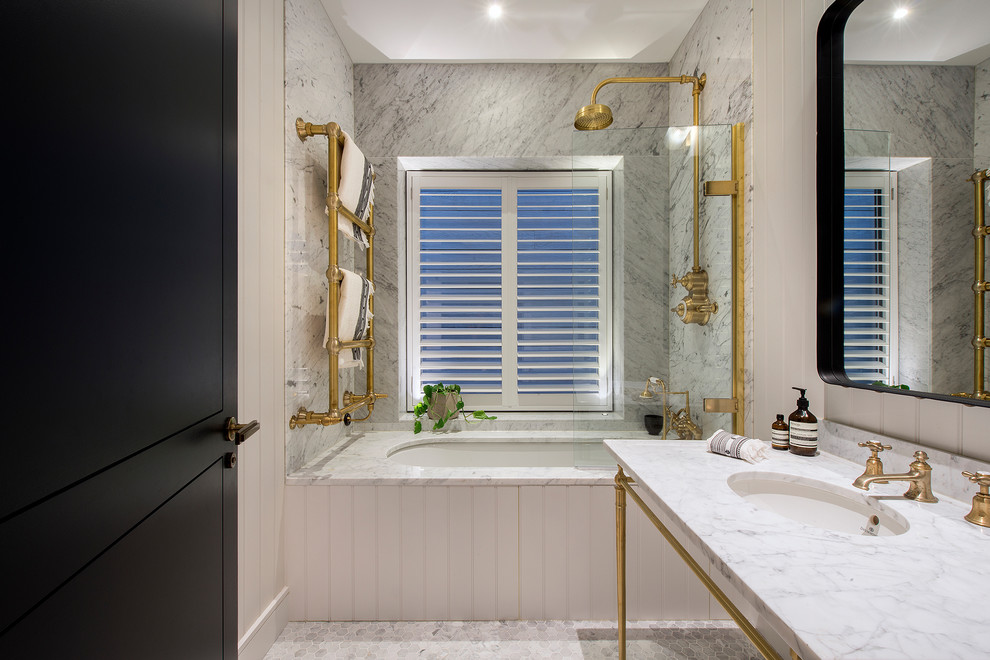 Photo of a mid-sized transitional 3/4 bathroom in London with a drop-in tub, a shower/bathtub combo, a console sink, marble benchtops, a hinged shower door, open cabinets, gray tile, beige walls, grey floor and marble floors.