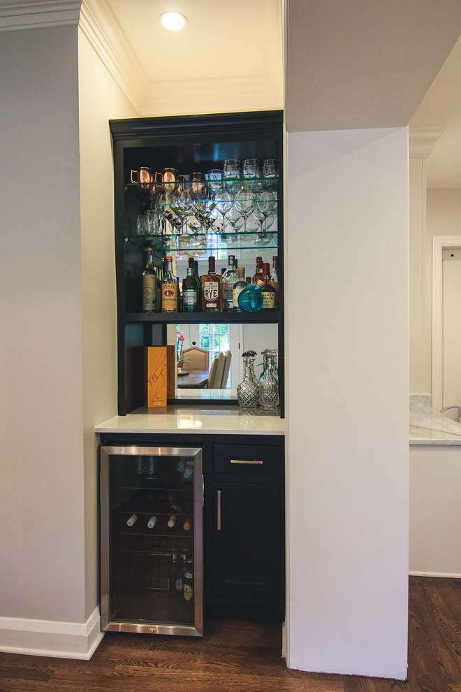 Photo of a small traditional single-wall wet bar in Baltimore with no sink, shaker cabinets, black cabinets, quartz benchtops, mirror splashback, medium hardwood floors and brown floor.