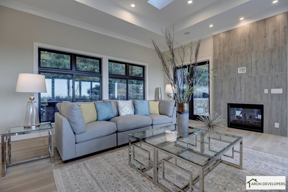 Inspiration for a large transitional open concept family room in San Francisco with beige walls, light hardwood floors, a two-sided fireplace, a tile fireplace surround, a wall-mounted tv, white floor and a game room.