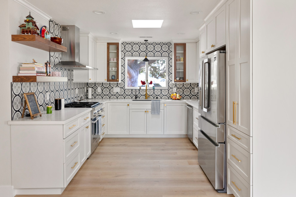 This is an example of a transitional u-shaped kitchen in San Francisco with an undermount sink, shaker cabinets, white cabinets, multi-coloured splashback, stainless steel appliances, light hardwood floors, no island, beige floor and white benchtop.
