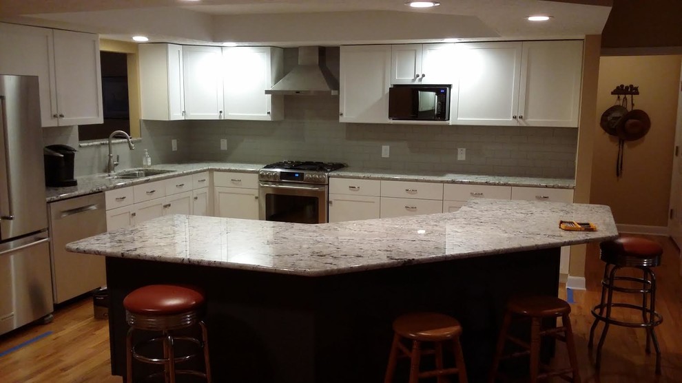 Inspiration for a mid-sized transitional l-shaped medium tone wood floor and brown floor open concept kitchen remodel with a double-bowl sink, shaker cabinets, white cabinets, granite countertops, gray backsplash, subway tile backsplash, stainless steel appliances and an island