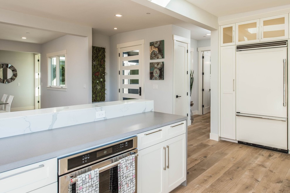 Open concept kitchen - large transitional u-shaped light wood floor open concept kitchen idea in Orange County with shaker cabinets, white cabinets, stone tile backsplash, no island, beige backsplash, stainless steel appliances and gray countertops