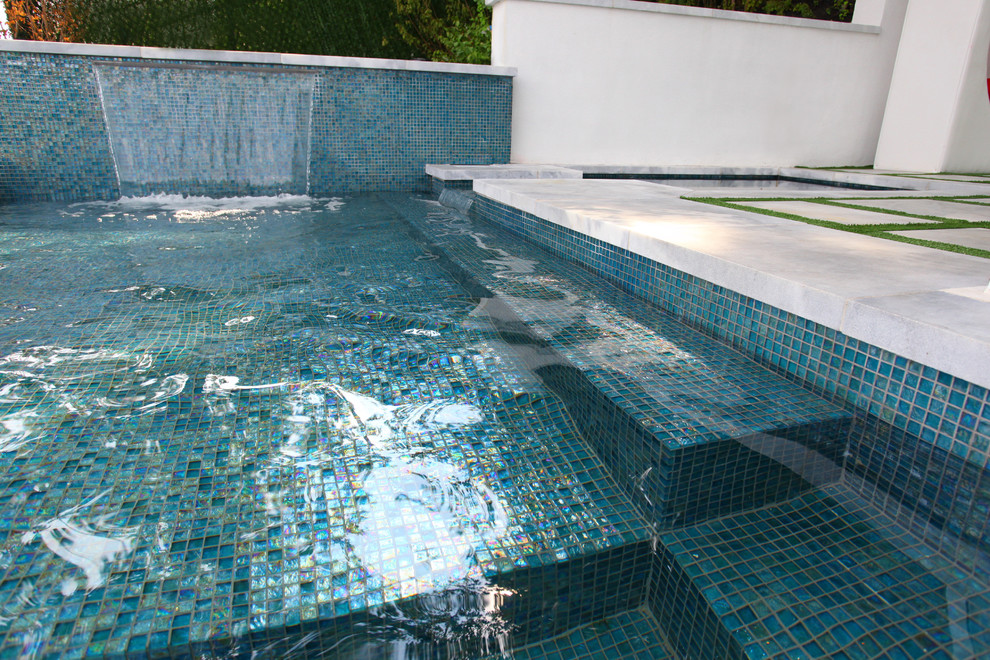 This is an example of a large modern backyard l-shaped lap pool in New York with a water feature and concrete slab.