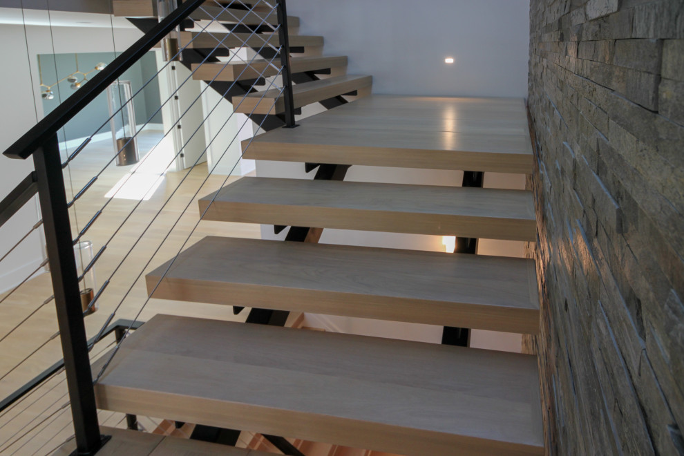 Aménagement d'un grand escalier flottant éclectique avec des marches en bois, un garde-corps en métal et un mur en parement de brique.
