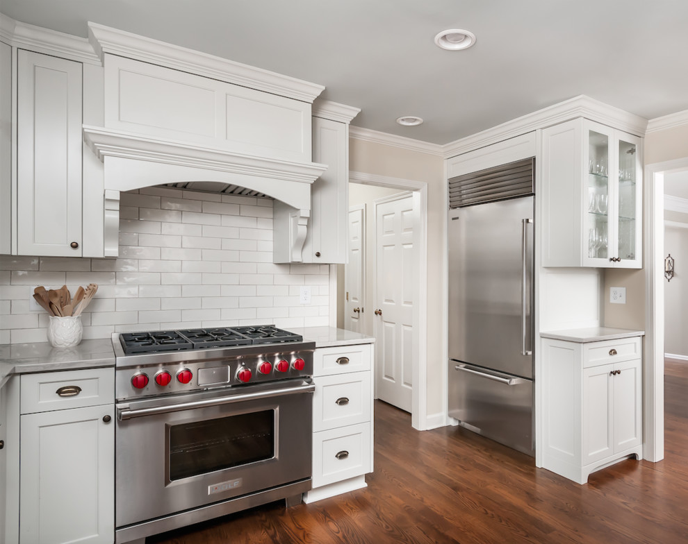 Inspiration for a mid-sized transitional kitchen in Atlanta with a farmhouse sink, shaker cabinets, white cabinets, quartzite benchtops, white splashback, ceramic splashback, stainless steel appliances, medium hardwood floors, no island, brown floor and white benchtop.