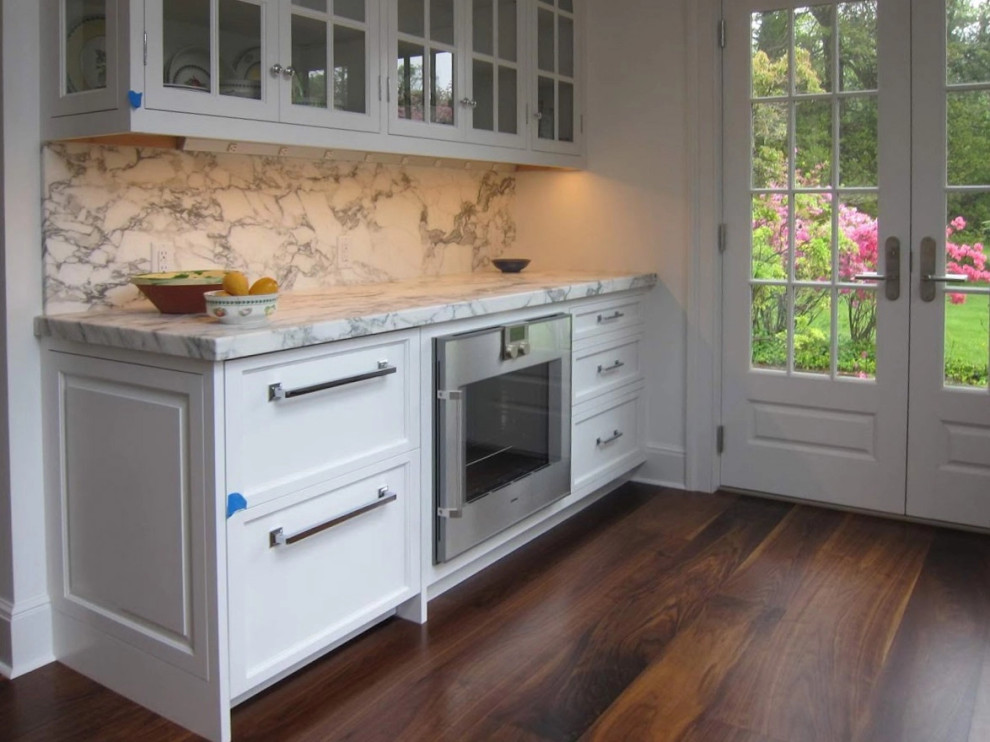 Inspiration for a traditional kitchen in New York with white cabinets, stainless steel appliances, dark hardwood floors and glass-front cabinets.