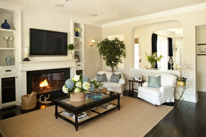 Inspiration for a mid-sized traditional open concept family room in Los Angeles with beige walls, dark hardwood floors, a standard fireplace, a wood fireplace surround and a wall-mounted tv.