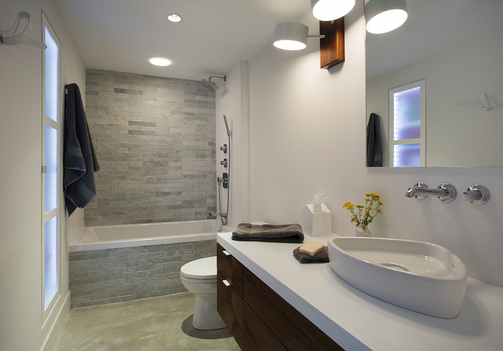 This is an example of a mid-sized contemporary master bathroom in Boston with a vessel sink, flat-panel cabinets, dark wood cabinets, engineered quartz benchtops, an alcove tub, a shower/bathtub combo, a one-piece toilet, gray tile, white walls, concrete floors and stone tile.