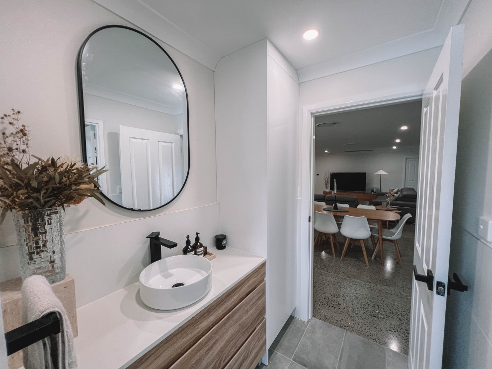 Design ideas for a mid-sized scandinavian powder room in Newcastle - Maitland with flat-panel cabinets, light wood cabinets, a one-piece toilet, white tile, ceramic tile, white walls, ceramic floors, a vessel sink, engineered quartz benchtops, grey floor, white benchtops, a freestanding vanity, wood and wood walls.