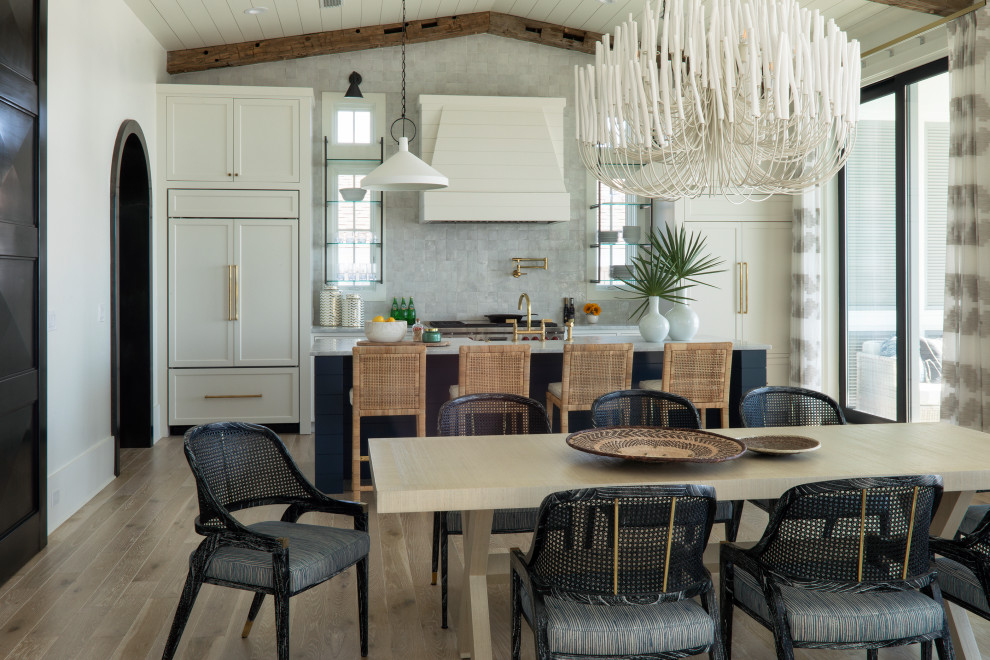 Large beach style single-wall painted wood floor, beige floor and exposed beam open concept kitchen photo in Other with a farmhouse sink, recessed-panel cabinets, white cabinets, granite countertops, gray backsplash, ceramic backsplash, white appliances, an island and gray countertops