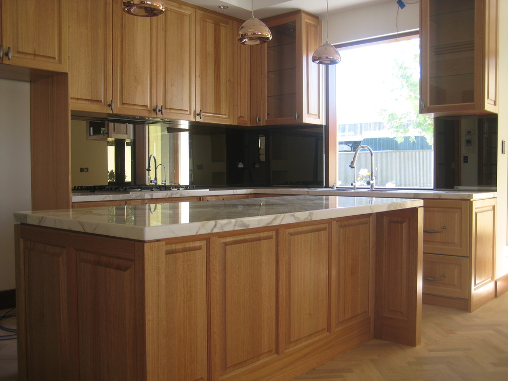 This is an example of a traditional l-shaped eat-in kitchen in Adelaide with raised-panel cabinets, medium wood cabinets, marble benchtops, mirror splashback and with island.