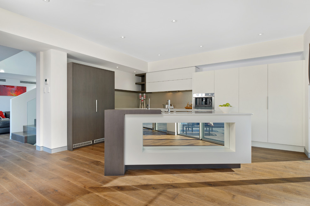 Mid-sized contemporary l-shaped eat-in kitchen in Sydney with flat-panel cabinets, white cabinets, beige splashback, panelled appliances, medium hardwood floors and with island.