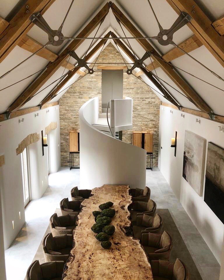 Expansive contemporary open plan dining in Gloucestershire with white walls, ceramic floors, a two-sided fireplace, a stone fireplace surround and white floor.