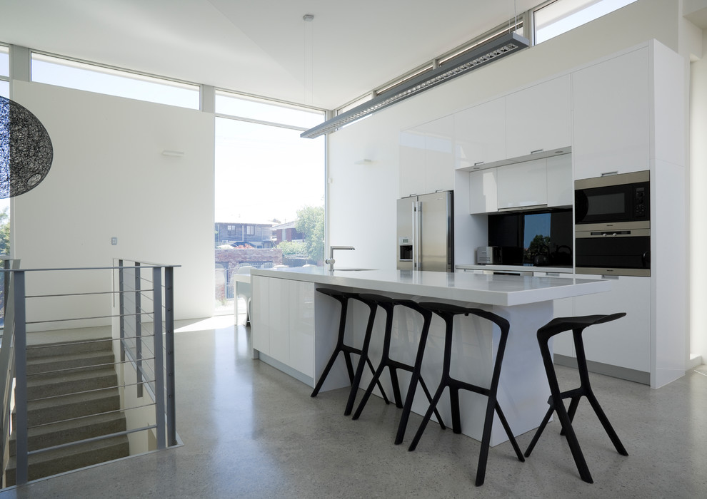 Photo of a contemporary galley kitchen in Perth with flat-panel cabinets, white cabinets, black splashback, glass sheet splashback, stainless steel appliances, terrazzo floors, with island and grey floor.