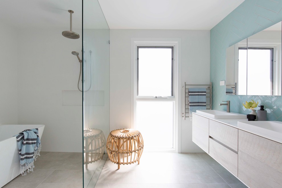 This is an example of a beach style 3/4 wet room bathroom in Sydney with flat-panel cabinets, light wood cabinets, a freestanding tub, blue tile, white walls, a drop-in sink, beige floor and an open shower.
