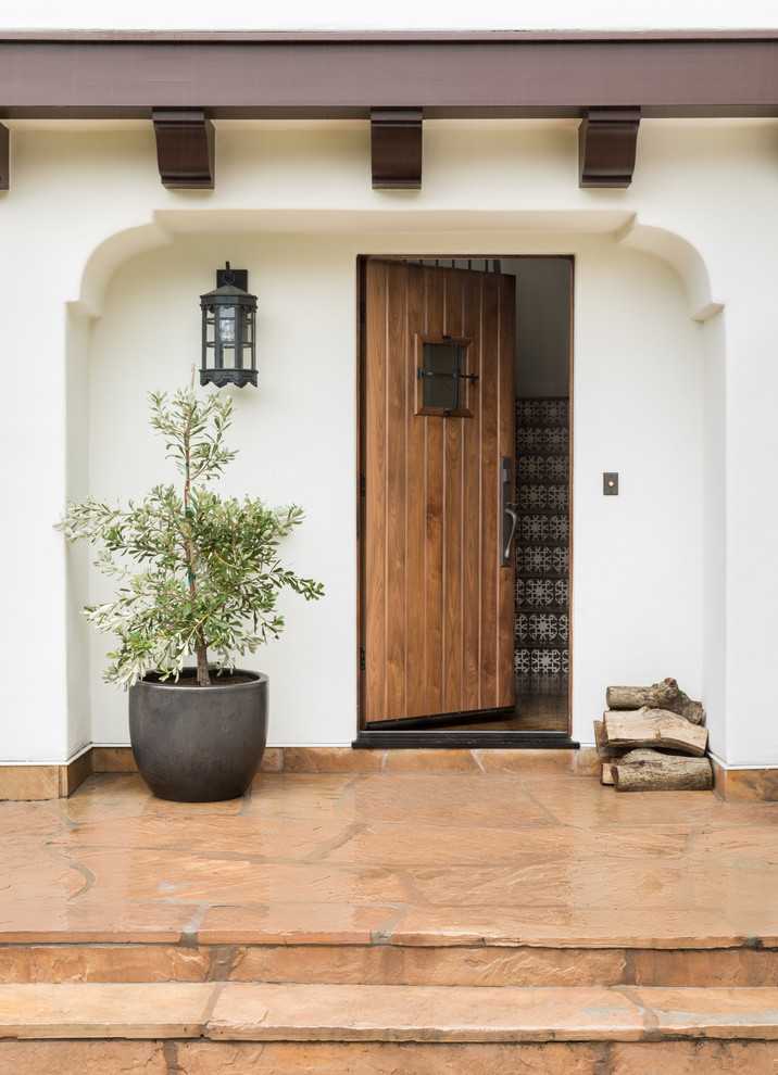 This is an example of a mediterranean front door in San Francisco with white walls, a single front door, a medium wood front door and orange floor.