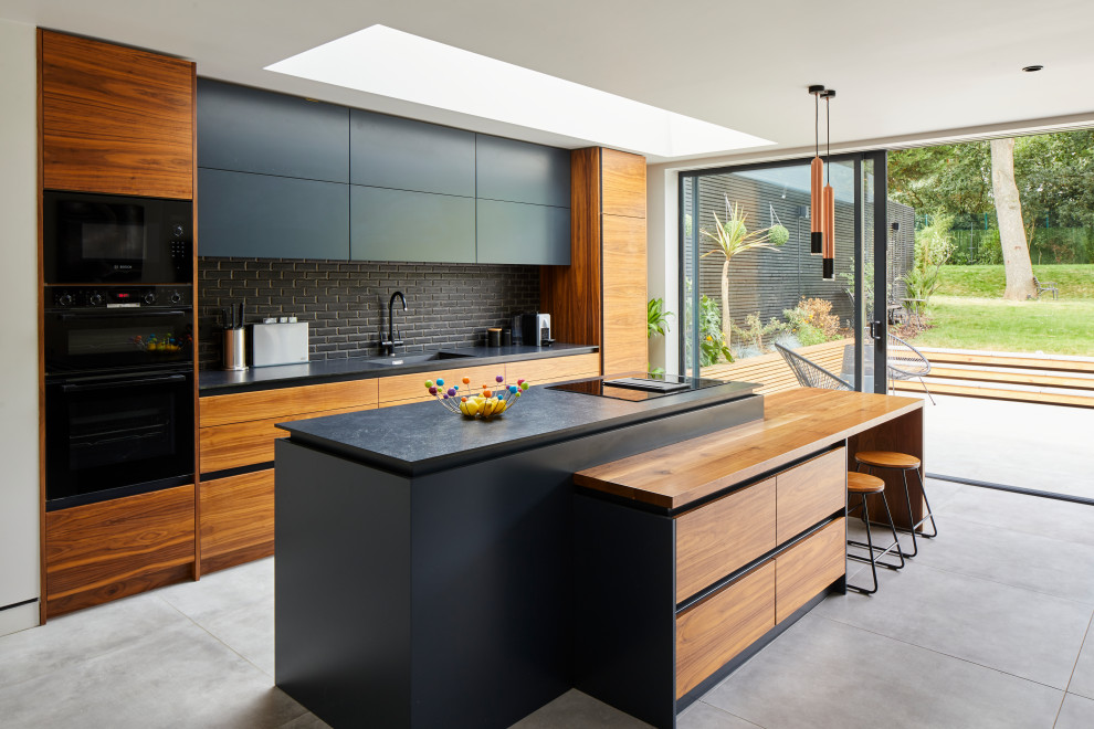 Inspiration for a contemporary kitchen in London with an integrated sink, flat-panel cabinets, black cabinets, black splashback, subway tile splashback, black appliances, with island, grey floor and black benchtop.