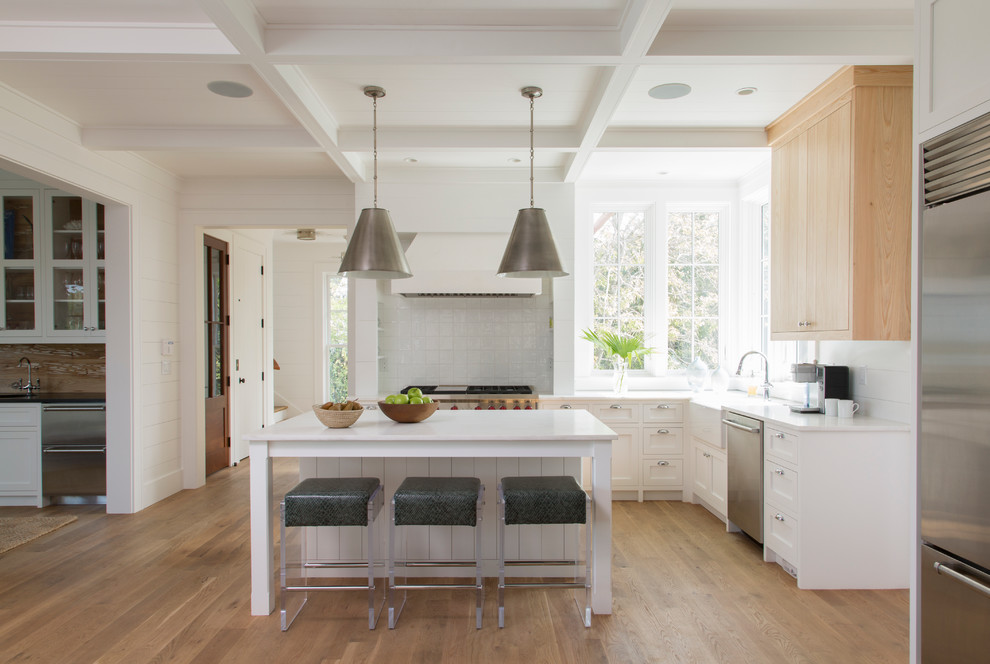 Beach style l-shaped kitchen in Charleston with a farmhouse sink, stainless steel appliances, with island, shaker cabinets, white cabinets, grey splashback and light hardwood floors.