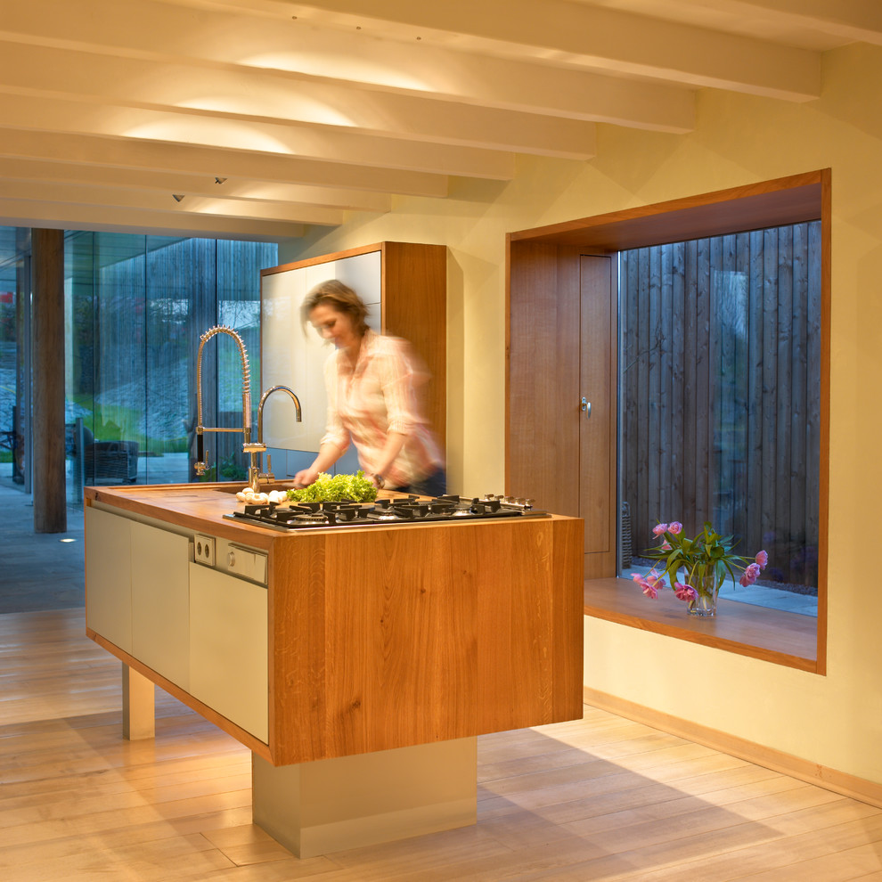 Küche mit flächenbündigen Schrankfronten, Arbeitsplatte aus Holz, schwarzen Elektrogeräten, zwei Kücheninseln, braunem Boden, integriertem Waschbecken, grauen Schränken, Küchenrückwand in Gelb, Rückwand aus Steinfliesen, gebeiztem Holzboden und brauner Arbeitsplatte in Cologne