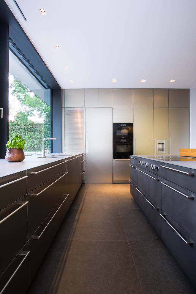 Offene, Große Moderne Küche in U-Form mit integriertem Waschbecken, flächenbündigen Schrankfronten, Schränken im Used-Look, Edelstahl-Arbeitsplatte, Küchenrückwand in Gelb, Rückwand-Fenster, schwarzen Elektrogeräten, Kücheninsel, grauem Boden und grauer Arbeitsplatte in Frankfurt am Main