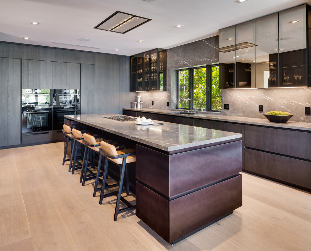 This is an example of a large contemporary kitchen in Miami with flat-panel cabinets, grey splashback, stone slab splashback, black appliances, light hardwood floors, with island, beige floor, a single-bowl sink, grey benchtop and dark wood cabinets.
