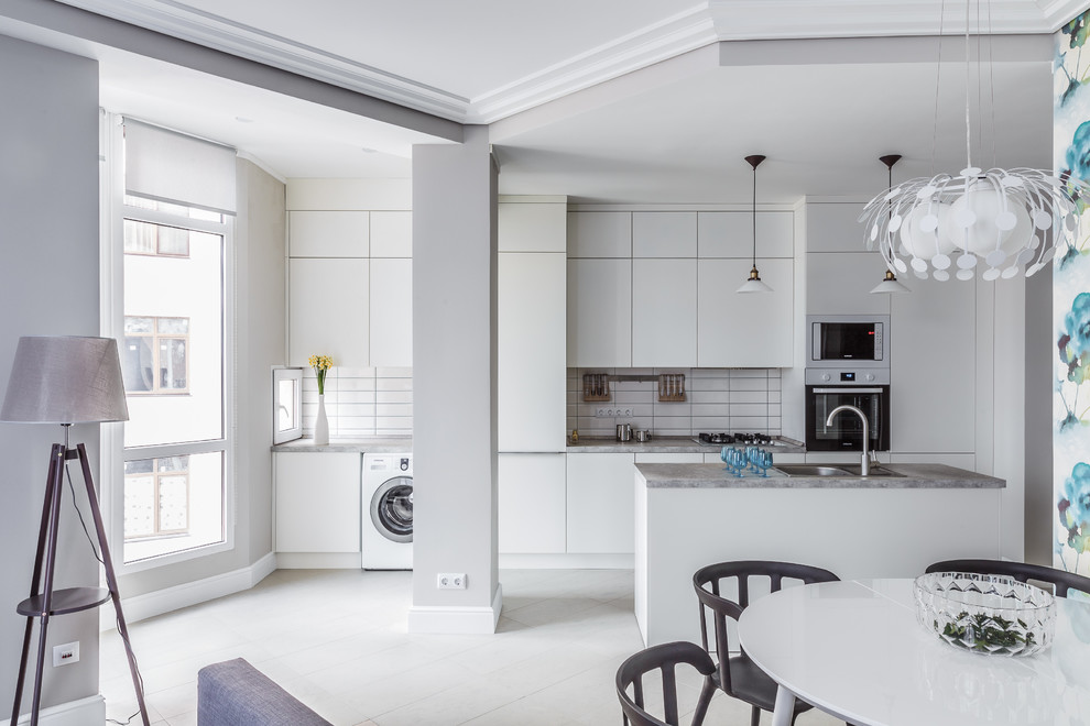 Inspiration for a contemporary galley open plan kitchen in Other with a drop-in sink, flat-panel cabinets, white cabinets, white splashback, white appliances, with island, white floor and subway tile splashback.