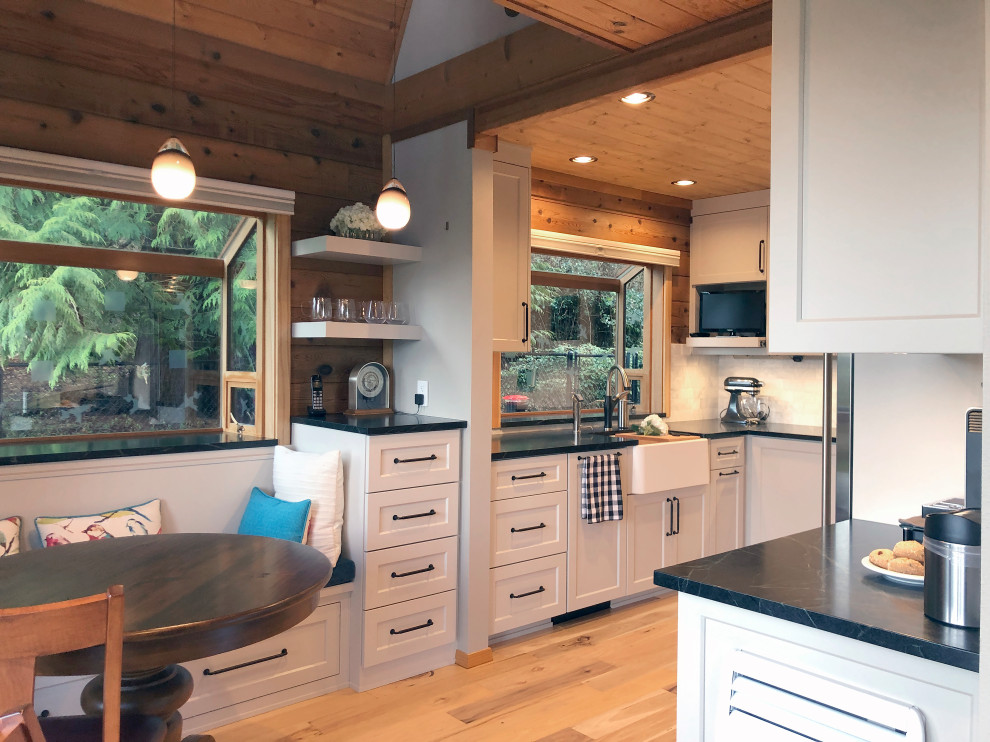 Mid-sized farmhouse l-shaped light wood floor, yellow floor and vaulted ceiling eat-in kitchen photo in Seattle with a farmhouse sink, shaker cabinets, gray cabinets, soapstone countertops, white backsplash, marble backsplash, stainless steel appliances and black countertops