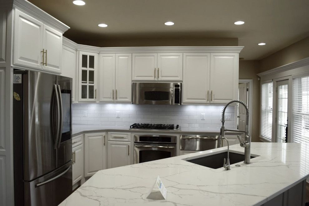 Large transitional l-shaped dark wood floor eat-in kitchen photo in Milwaukee with an undermount sink, raised-panel cabinets, white cabinets, white backsplash, stainless steel appliances, an island and multicolored countertops