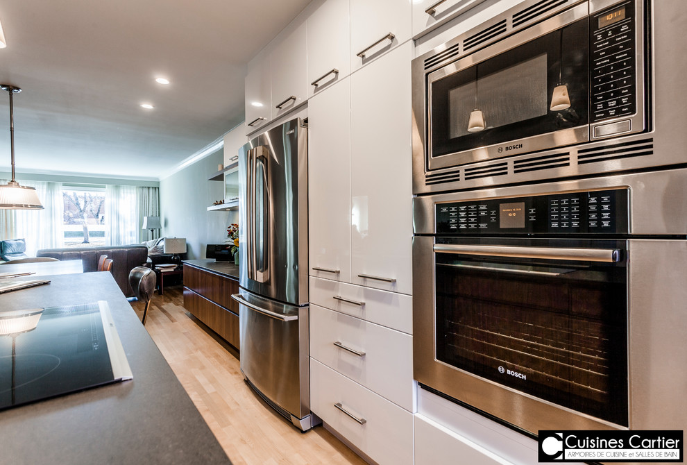 Eat-in kitchen - large transitional galley medium tone wood floor eat-in kitchen idea in Montreal with an undermount sink, flat-panel cabinets, dark wood cabinets, quartzite countertops, white backsplash, mosaic tile backsplash, stainless steel appliances and an island