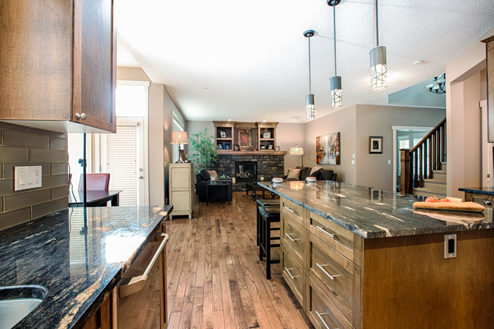 Inspiration for a mid-sized rustic u-shaped medium tone wood floor and brown floor eat-in kitchen remodel in Calgary with an undermount sink, shaker cabinets, medium tone wood cabinets, granite countertops, gray backsplash, glass tile backsplash, stainless steel appliances and an island