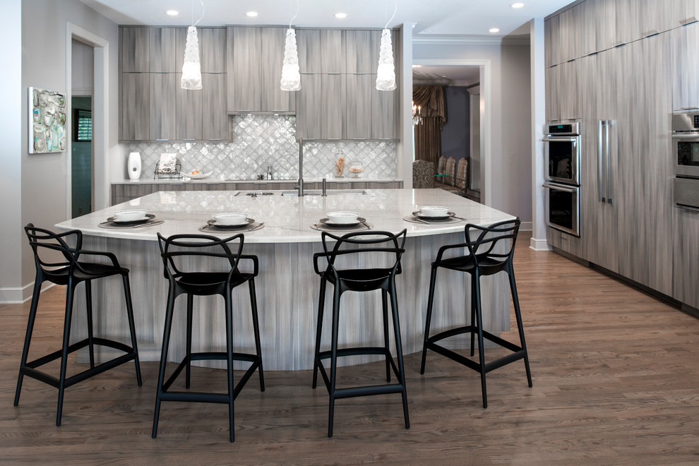 Inspiration for a large transitional medium tone wood floor and brown floor open concept kitchen remodel with an undermount sink, flat-panel cabinets, brown cabinets, quartzite countertops, white backsplash, ceramic backsplash, stainless steel appliances, an island and beige countertops
