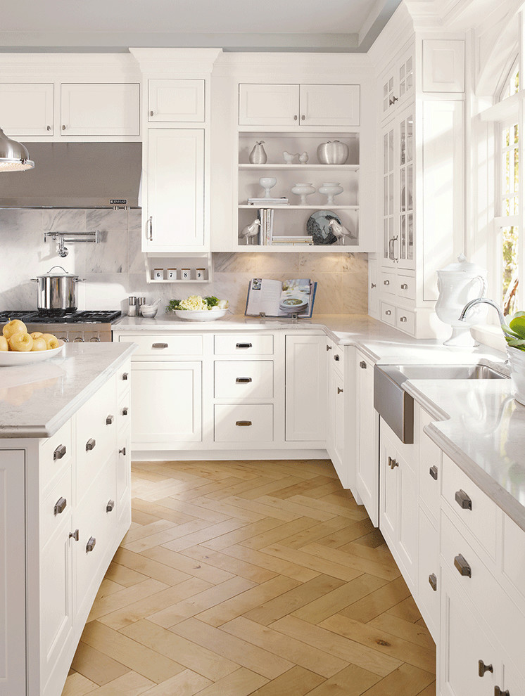 Large transitional l-shaped light wood floor and brown floor eat-in kitchen photo in New York with beaded inset cabinets, white cabinets, stainless steel appliances, an island, a farmhouse sink, quartz countertops, white backsplash, stone slab backsplash and gray countertops