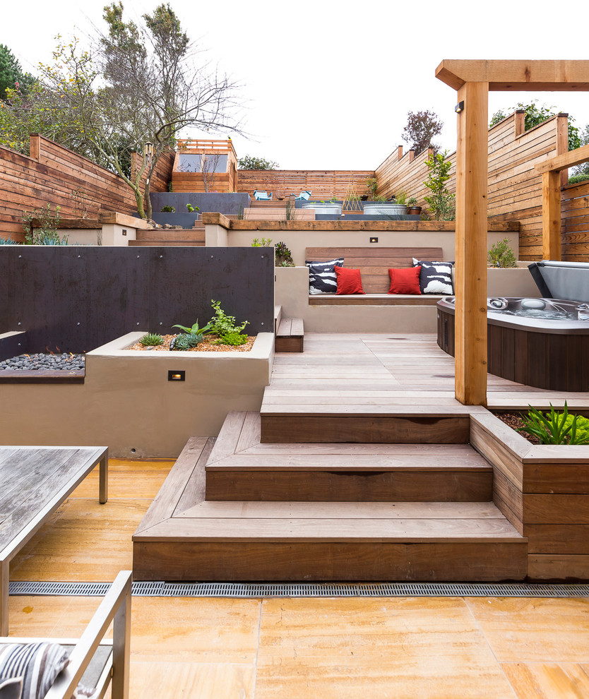 This is an example of a large contemporary backyard full sun garden in San Francisco with a retaining wall and decking.
