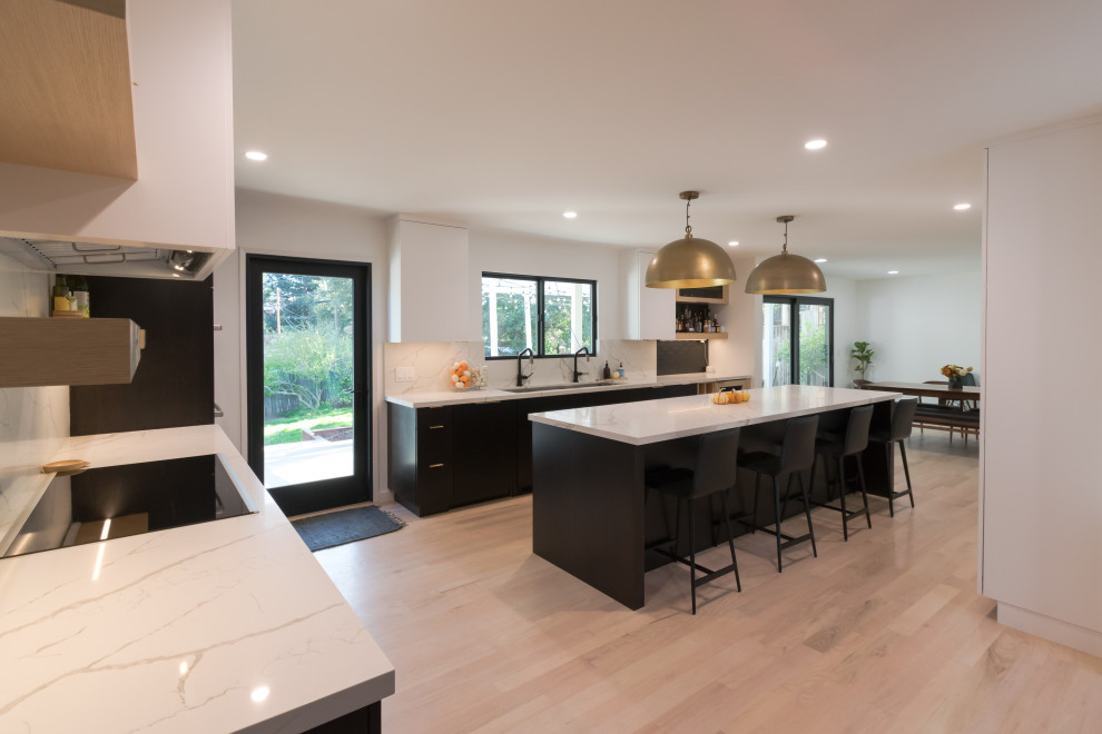 This is an example of a large modern u-shaped kitchen in San Francisco with a submerged sink, flat-panel cabinets, black cabinets, engineered stone countertops, white splashback, engineered quartz splashback, integrated appliances, light hardwood flooring, an island and white worktops.