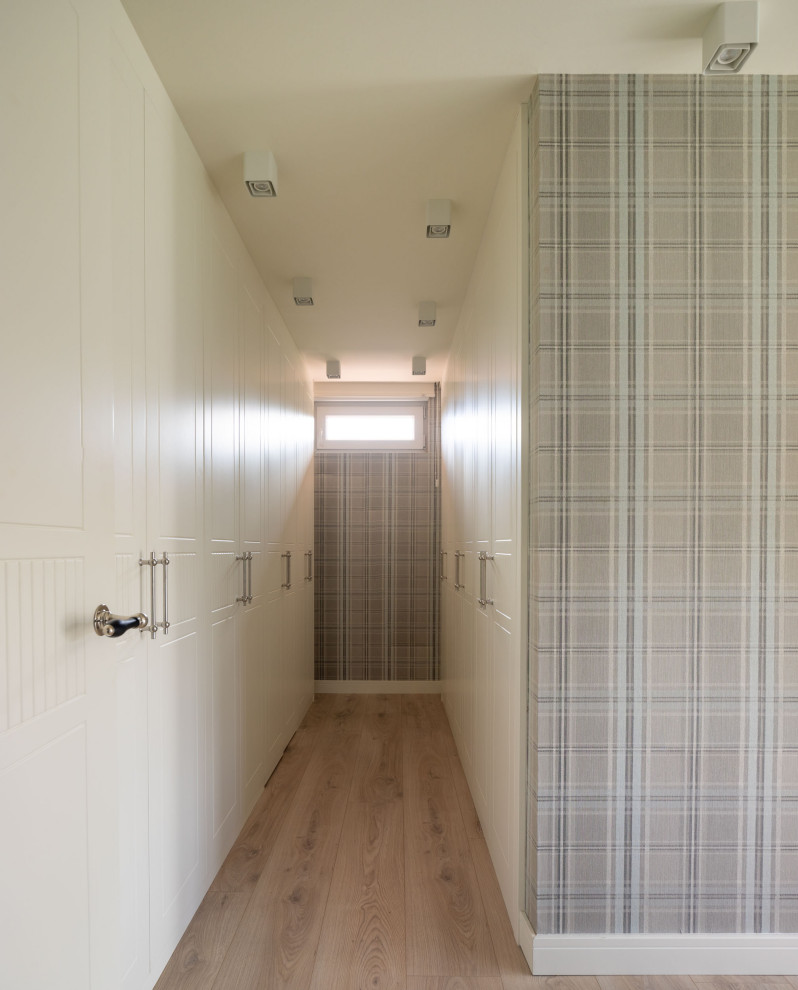 Cette image montre un grand dressing room traditionnel neutre avec un placard avec porte à panneau surélevé, des portes de placard blanches et sol en stratifié.