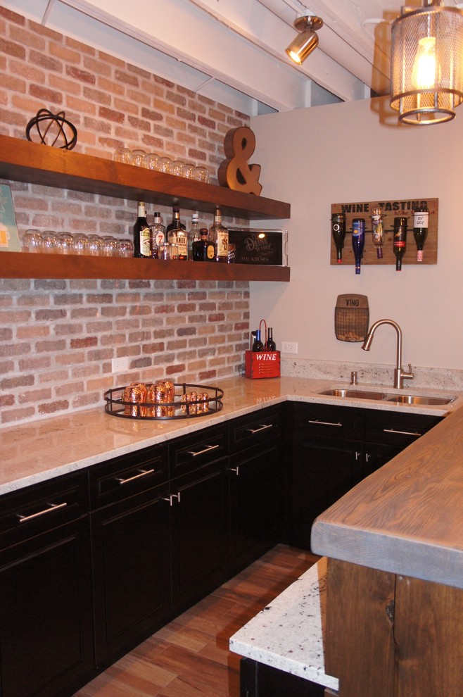Mid-sized country u-shaped wet bar in Chicago with an undermount sink, recessed-panel cabinets, granite benchtops, multi-coloured splashback, brick splashback, ceramic floors, dark wood cabinets and brown floor.