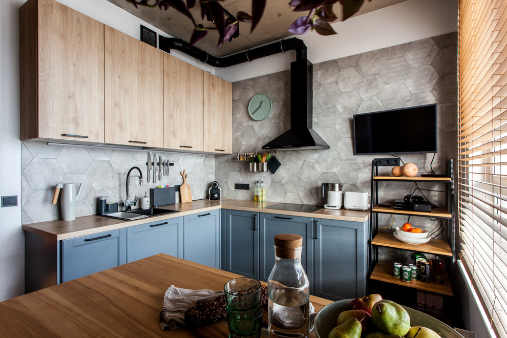 Photo of a contemporary l-shaped eat-in kitchen in Moscow with a drop-in sink, shaker cabinets, blue cabinets, wood benchtops, grey splashback, cement tile splashback, black appliances and brown benchtop.