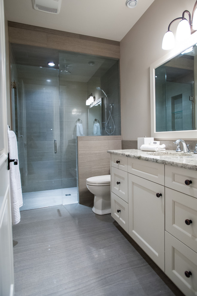 Photo of a mid-sized traditional bathroom in Calgary with shaker cabinets, white cabinets, a curbless shower, porcelain tile, grey walls, porcelain floors, an undermount sink, granite benchtops, a one-piece toilet and gray tile.